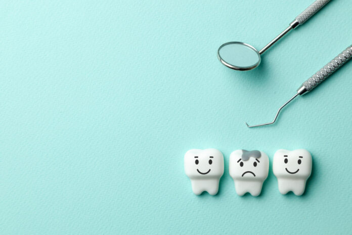 Healthy white teeth are smiling and tooth with caries is sad on green mint background and dentist tools mirror, hook. Copy space for text.